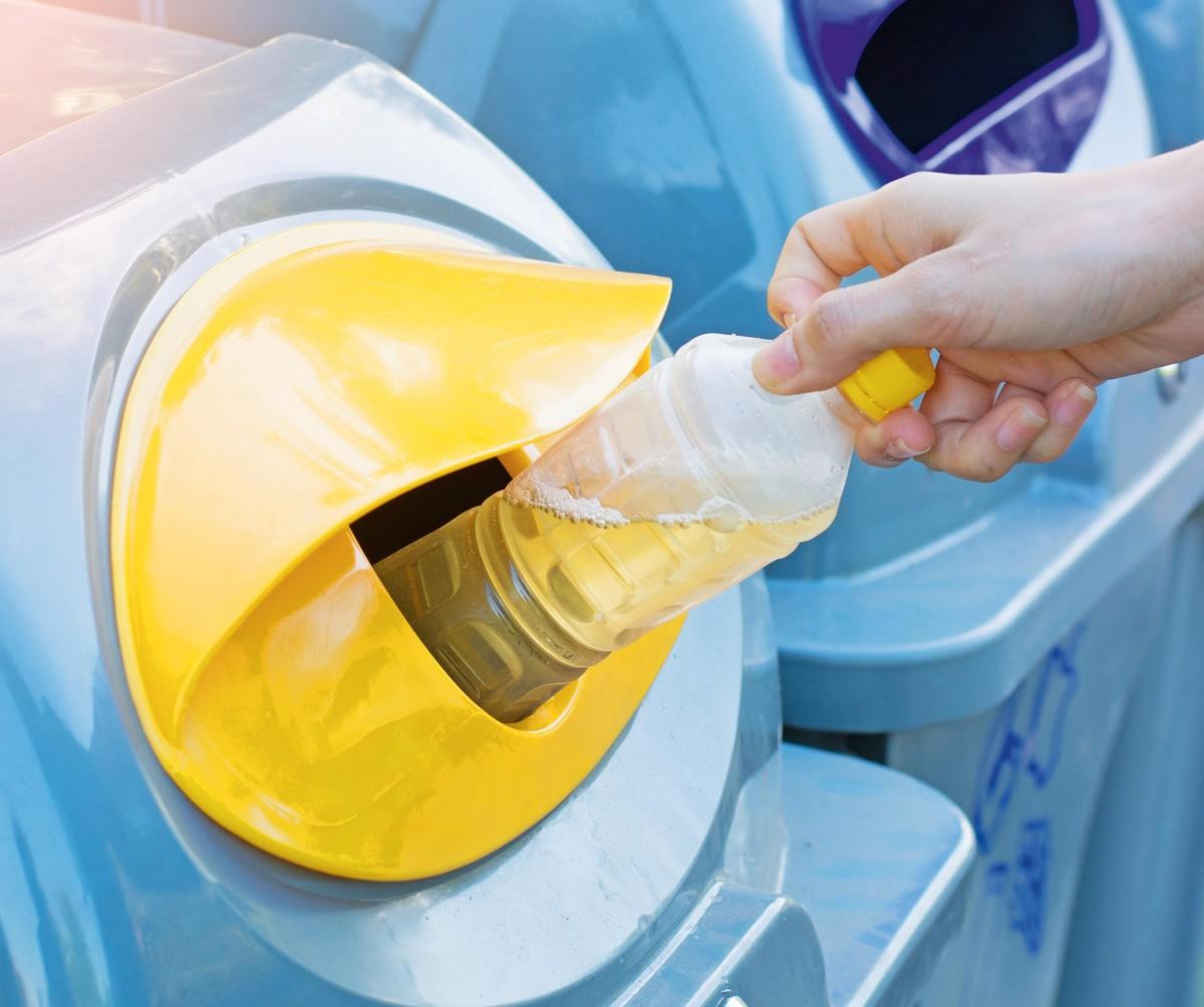 Photographie d'une personne jetant une bouteille plastique dans une poubelle de tri jaune.