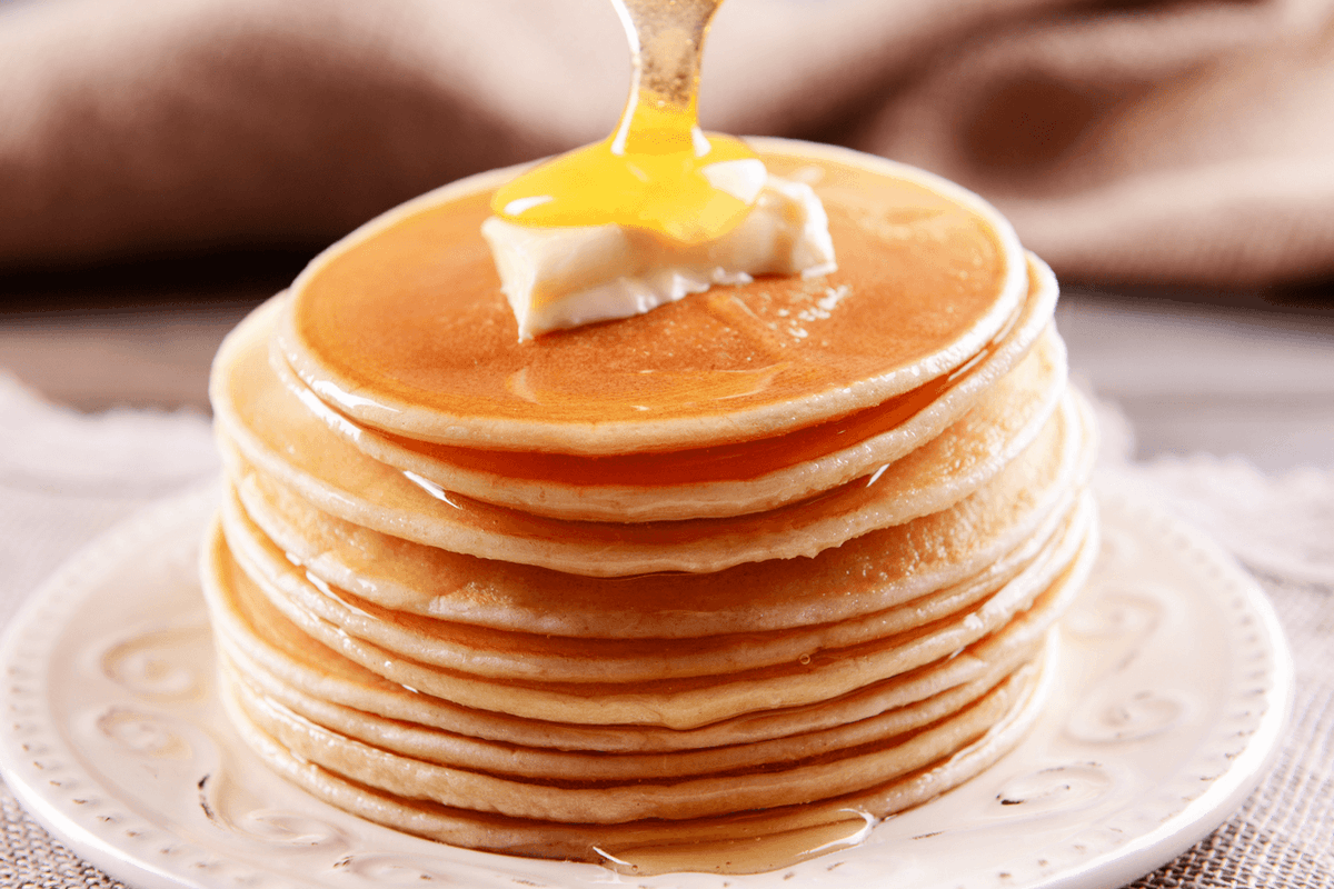 Photographie d'une pile de pancake sur laquelle on fait couler du miel