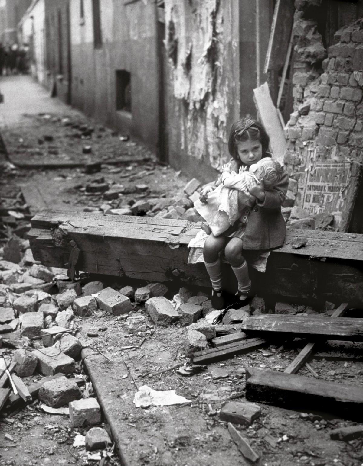 Une petite fille rassure sa poupée dans les décombres de sa maison bombardée