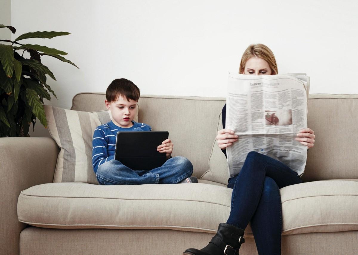Un jeune garçon utilisant une tablette, une mère lisant le journal